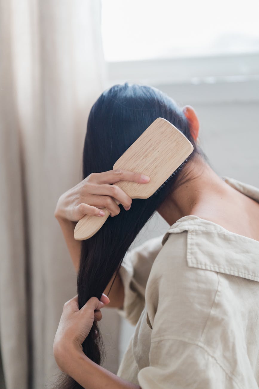 Woman with long dark hair brushing in a sunlit room, highlighting haircare routine.