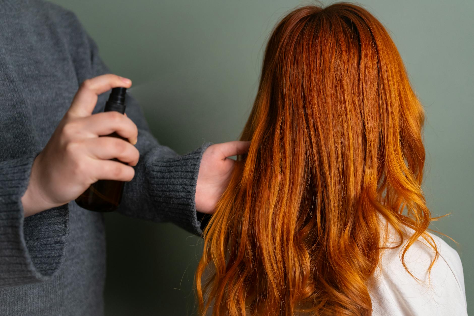 Close-up of hairdresser spraying hair product on long red hair.
